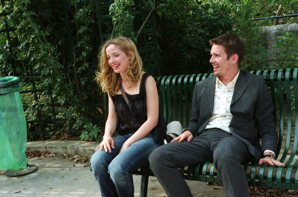 Before Sunset (2004) film still of Celine and Jesse sat on a green beach on Promenade Plantee in Paris