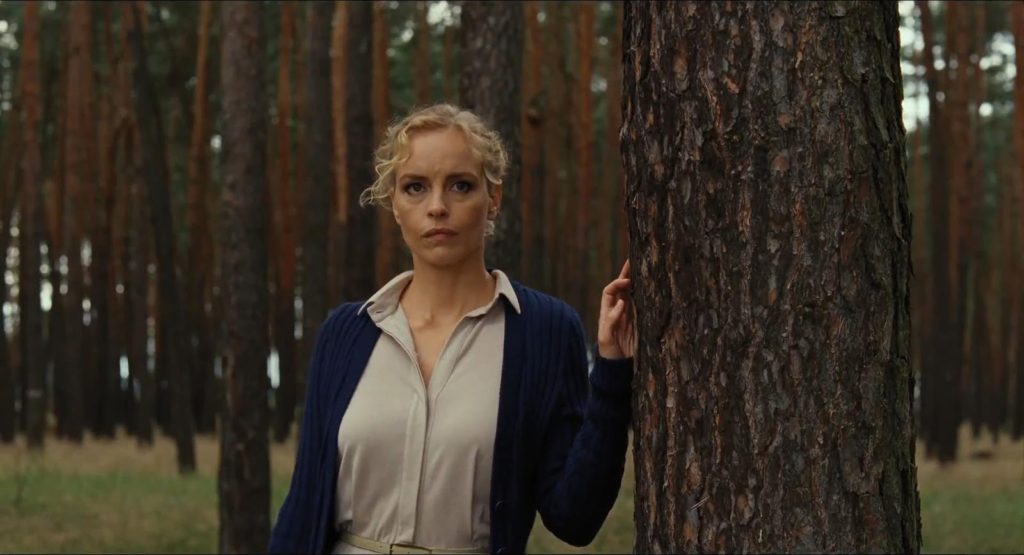 Film still from Barbara (2012) of a blonde woman leaning against a tree