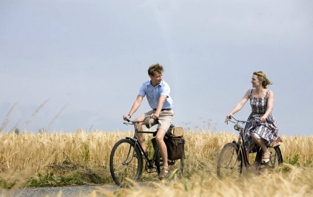 Film still from The Reader (2008), a movie set in Germany, of a young man and older woman cycling through the countryside