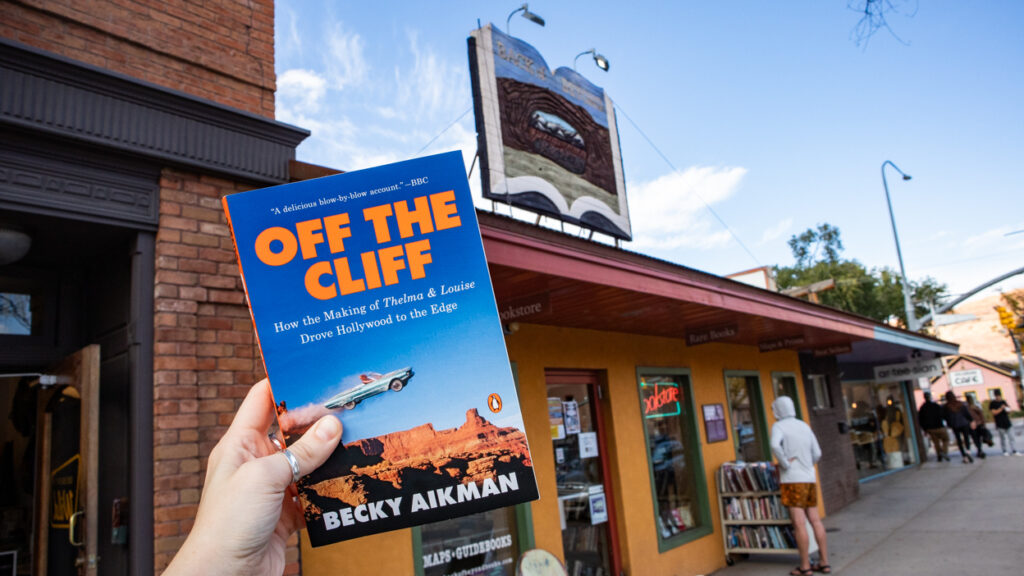 Off the Cliff by Becky Aikman book held in front of Back of Beyond Bookstore in Moab, Utah